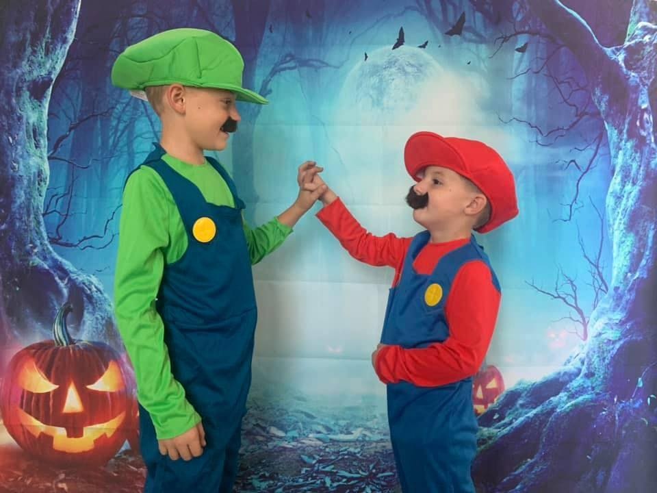 Mario and Luigi costumes Two boys dressed as Mario and Luigi holding hands smiling in front of a spooky backdrop.